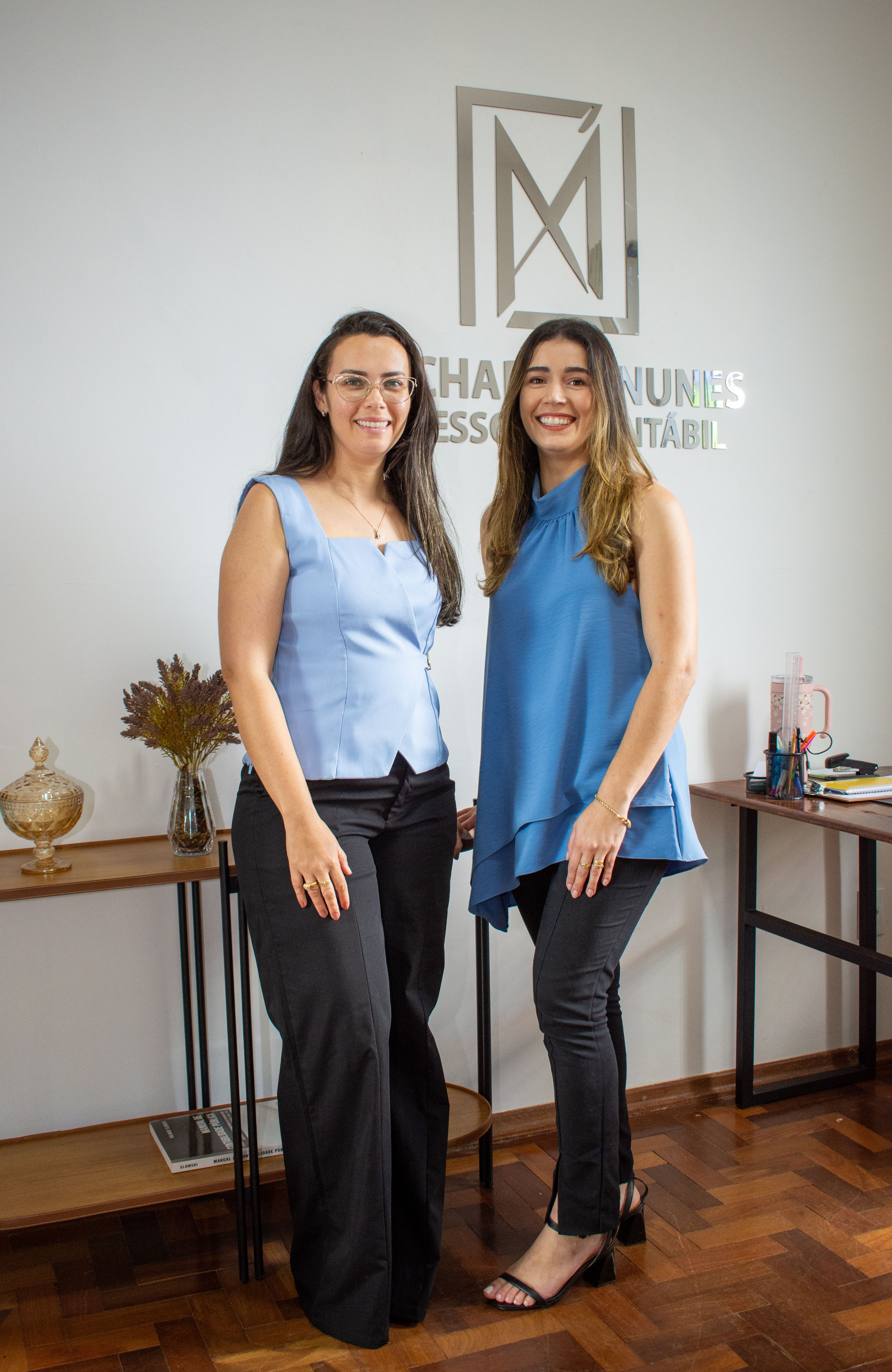 Two smiling women in business attire standing in a modern office.