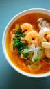 Top view of white bowl with delicious soup Tom Yam placed on blue table