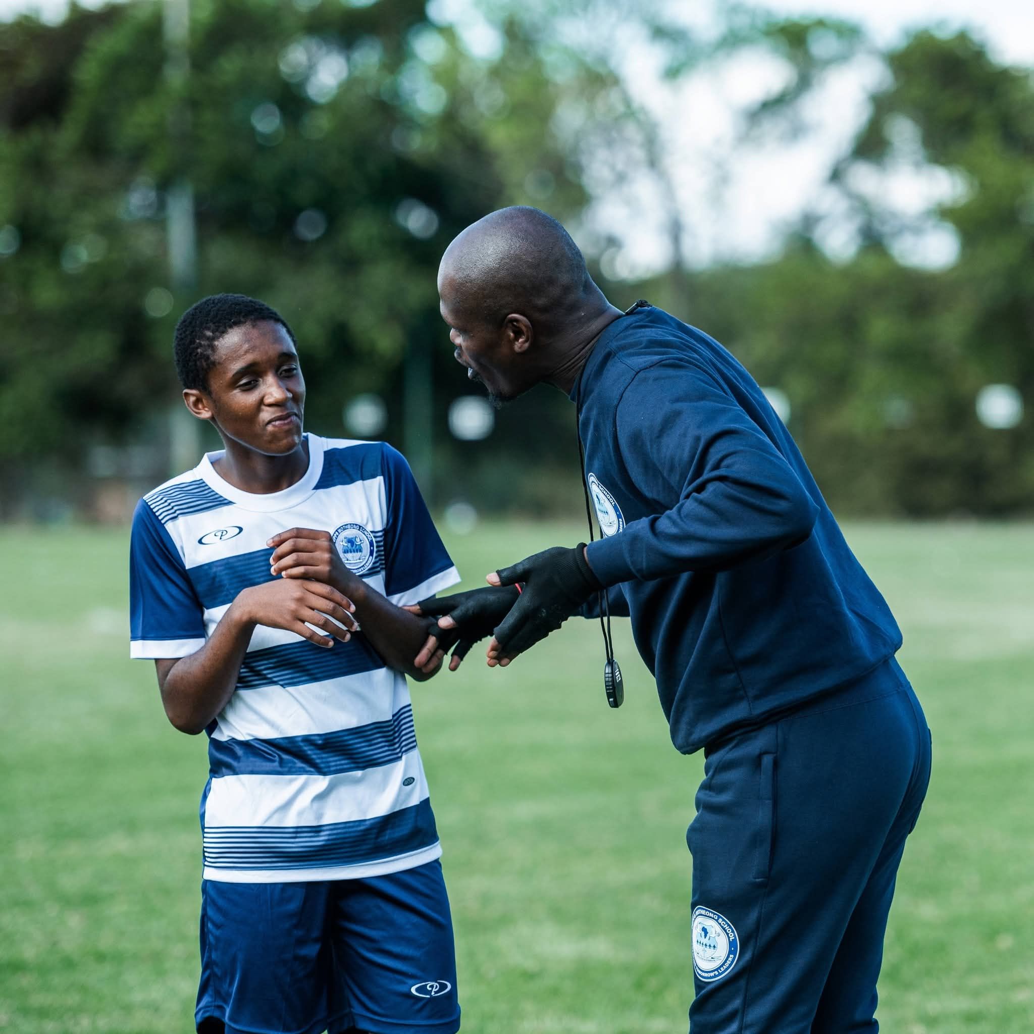 Coach giving instructions to a young soccer player on a grassy field.