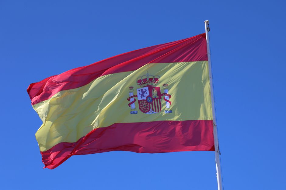 Vibrante bandera de España ondeando al viento con un fondo de cielo azul claro, mostrando orgullo nacional.