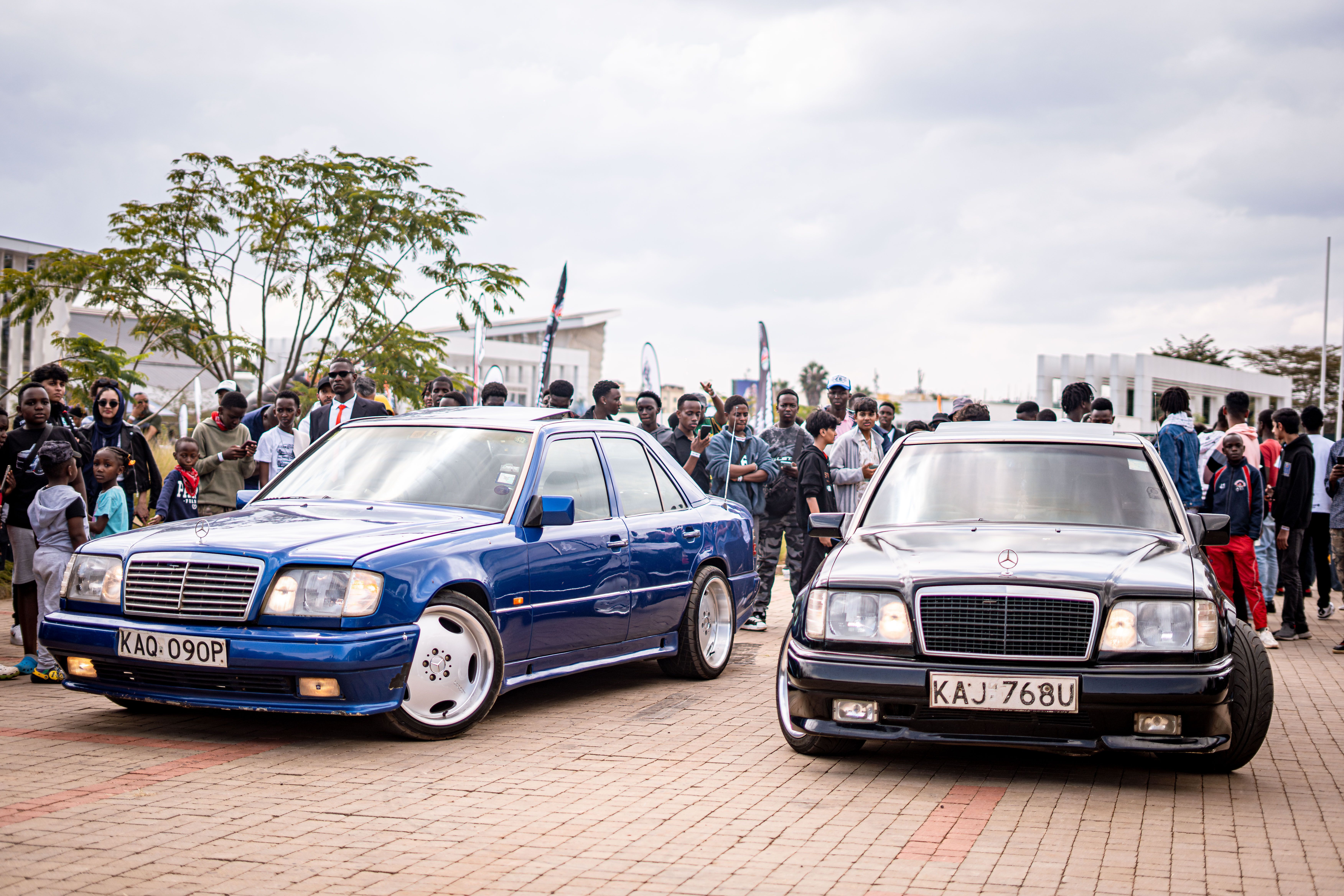 Two classic Mercedes-Benz cars displayed at an outdoor car show with a crowd of onlookers.