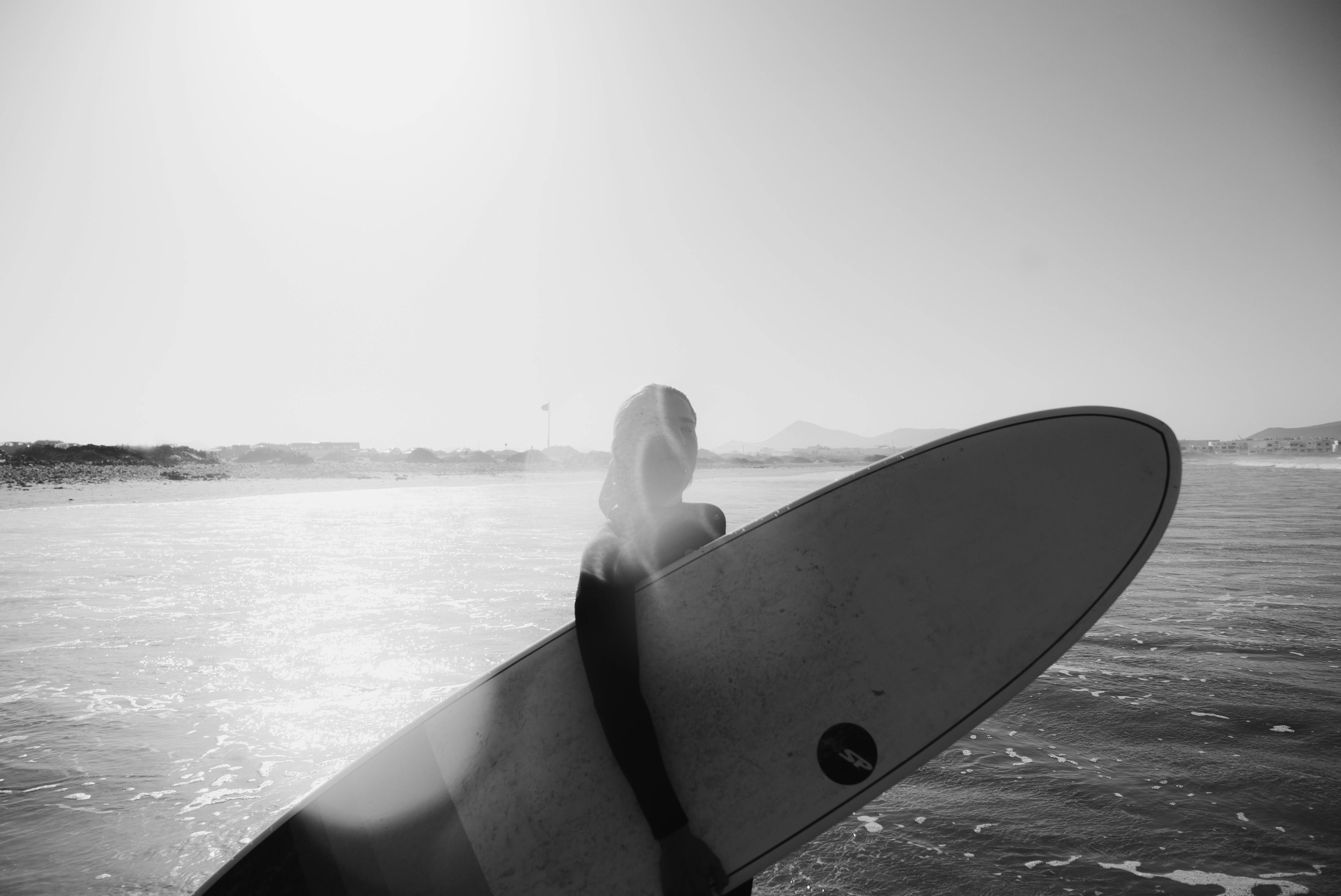 anonymous man carrying surfboard on seafront