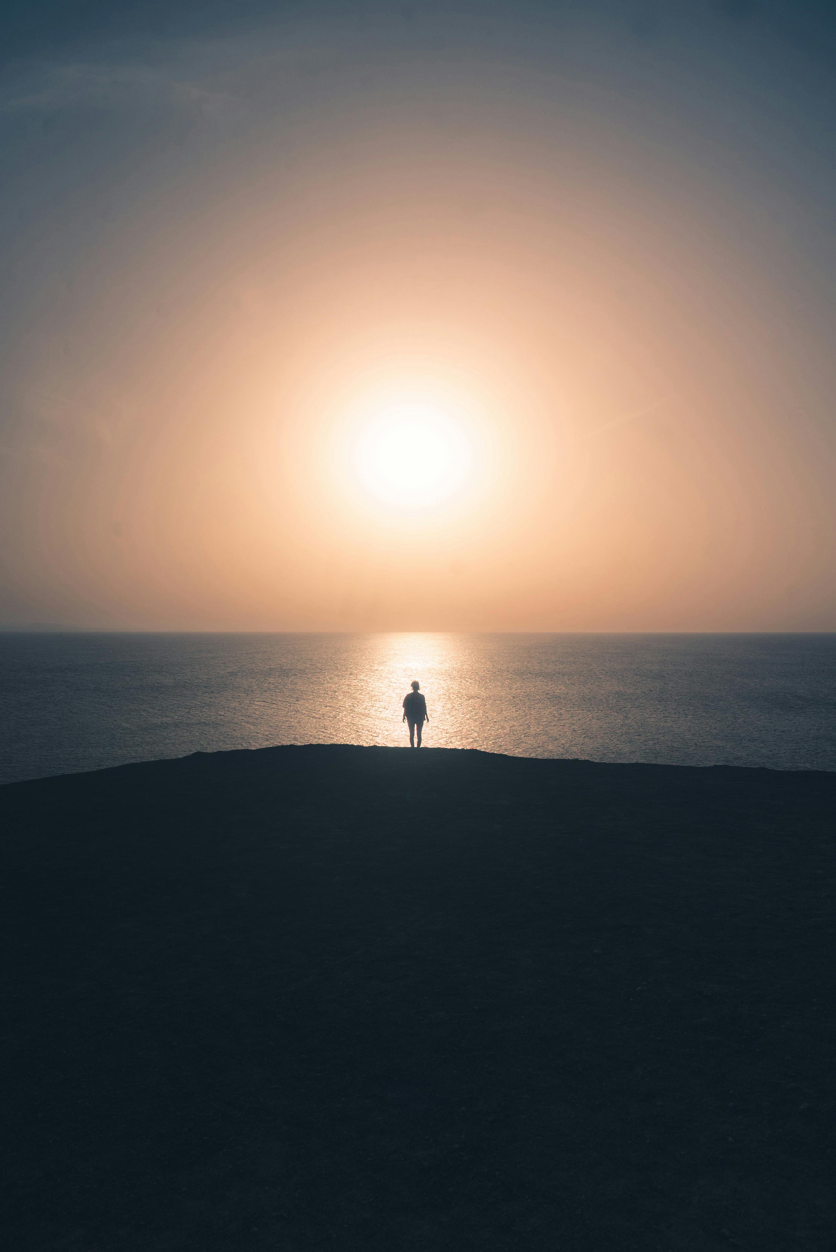一个孤独的人影站在广阔的海洋地平线上，映衬着炽热的日落，创造出一个宁静的轮廓