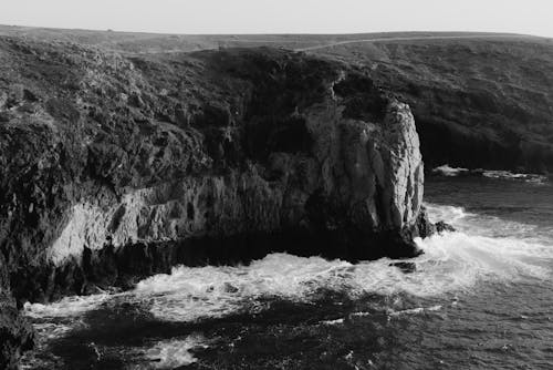 Black and white amazing aerial view of rocky coastline and foamy sea waves rolling to rocky cliff on daytime