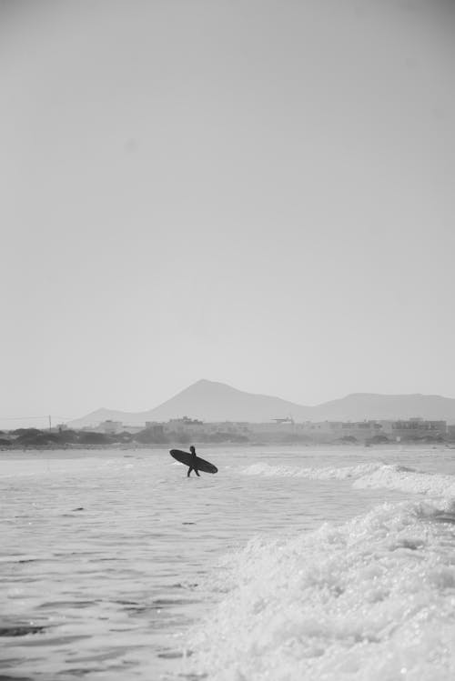 Foto In Scala Di Grigi Della Persona Che Trasporta La Tavola Da Surf Che Cammina Sull'acqua