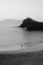 一个孤独的人沿着宁静的海滩漫步，海滩上有岩石悬崖，照片以单色拍摄