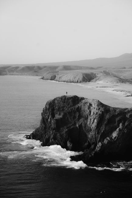 Black and white view of a rugged coastal cliff with crashing waves.