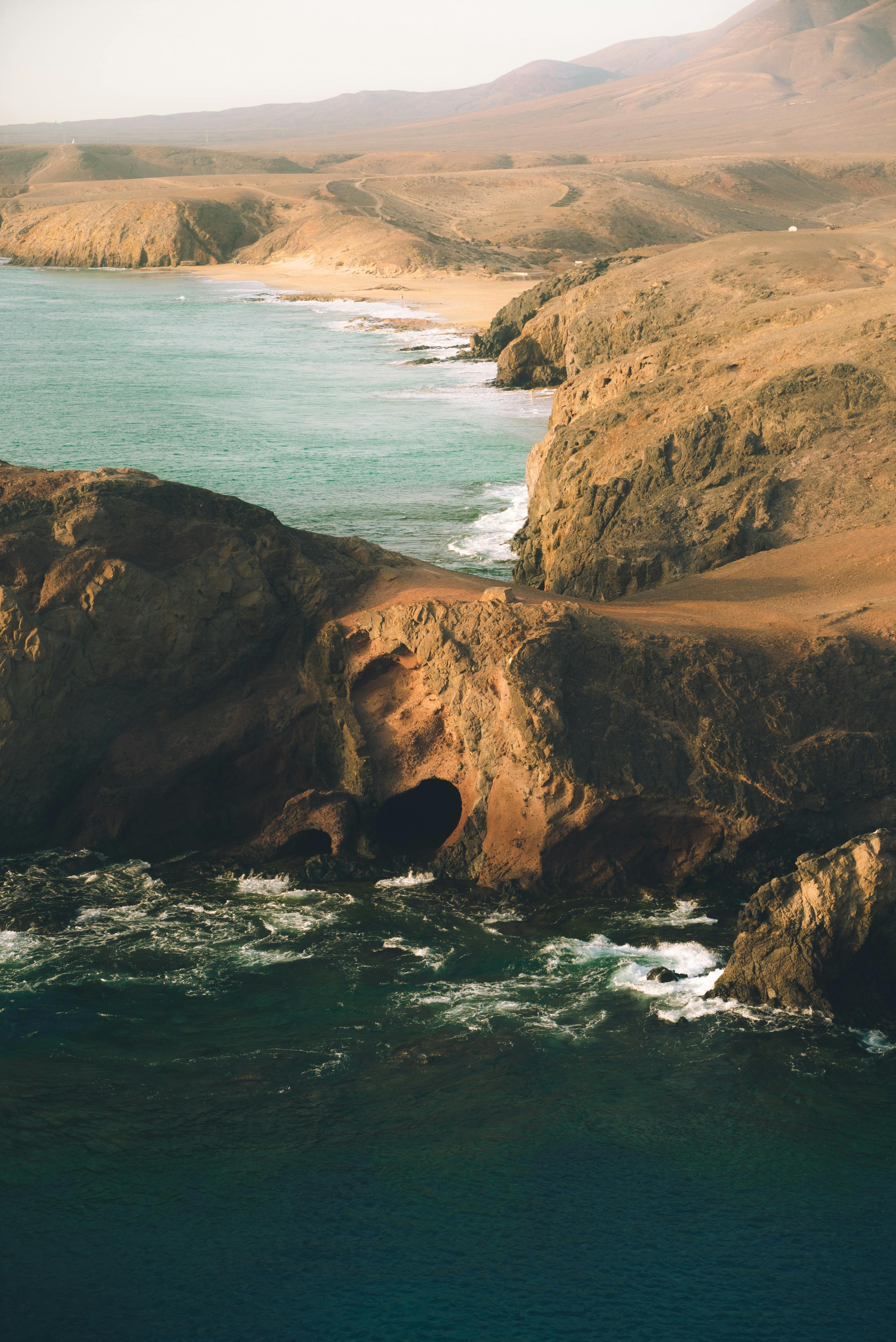 从鸟瞰视角看，崎岖的海岸线与日落时的海浪相碰撞，完美融合了旅行与自然主题