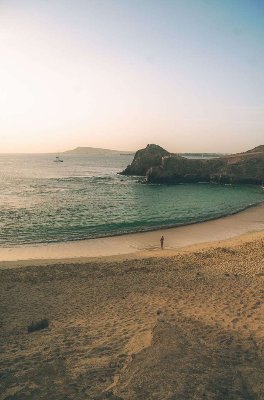 Person walking along a beach at sunset