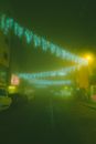 Illuminated city street with parked cars and decorated with glowing garlands covered with fog at dark night