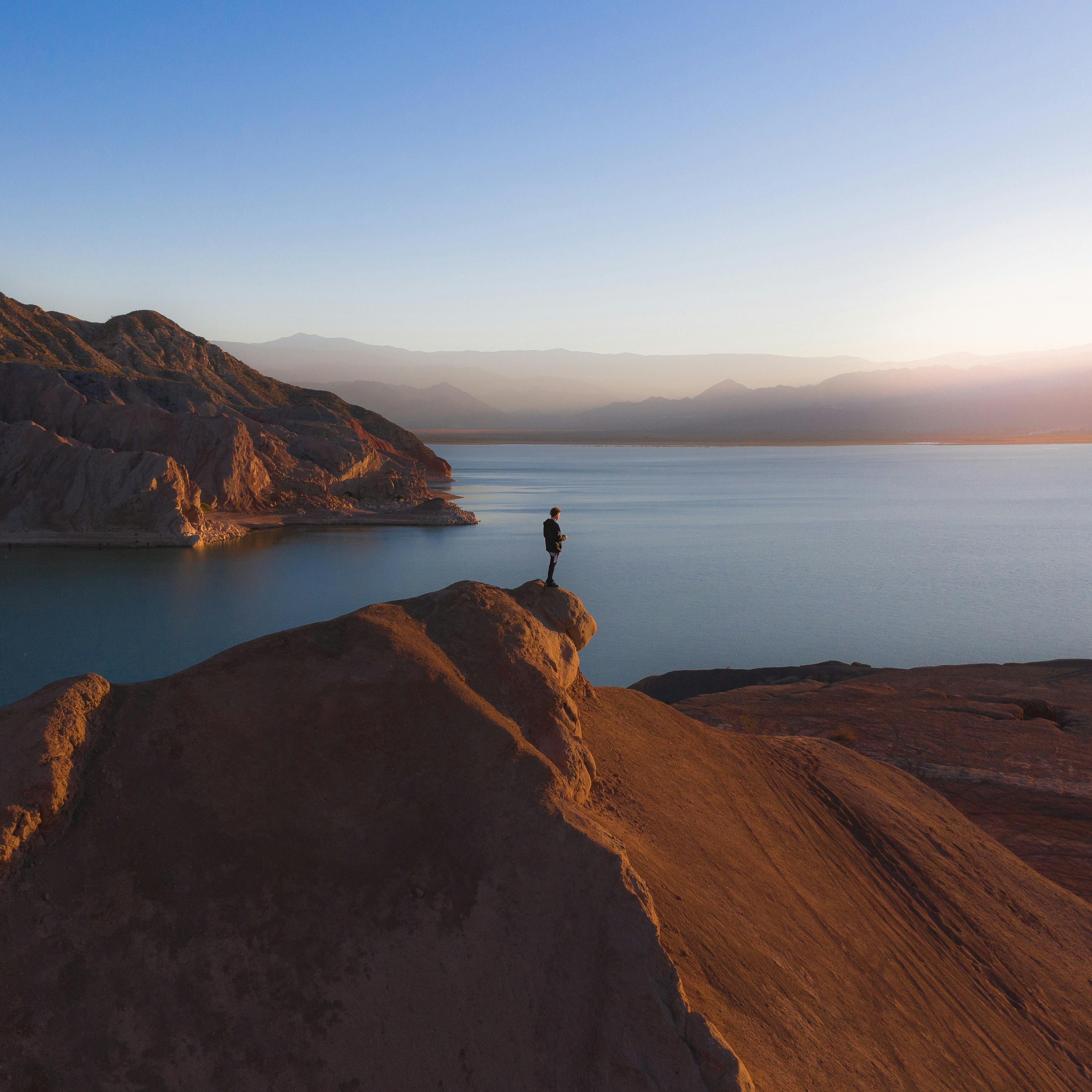 person standing on brown rock formation near body of water