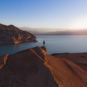 A lone hiker on a rocky peak above a lake at sunrise — Tomas Anunziata on Pexels