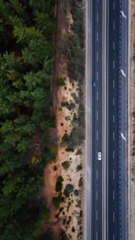Aerial shot of a highway cutting through a dense forest, capturing the essence of travel and nature.