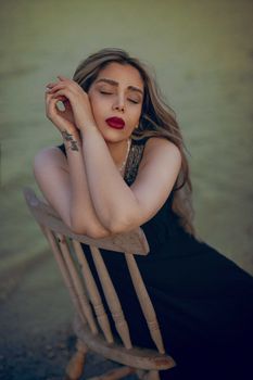 Portrait of woman with serene expression sitting on chair outdoors, eyes closed, in a reflective mood.