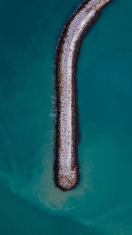 Aerial top view of breakwater with pier in clear turquoise water of ocean lagoon