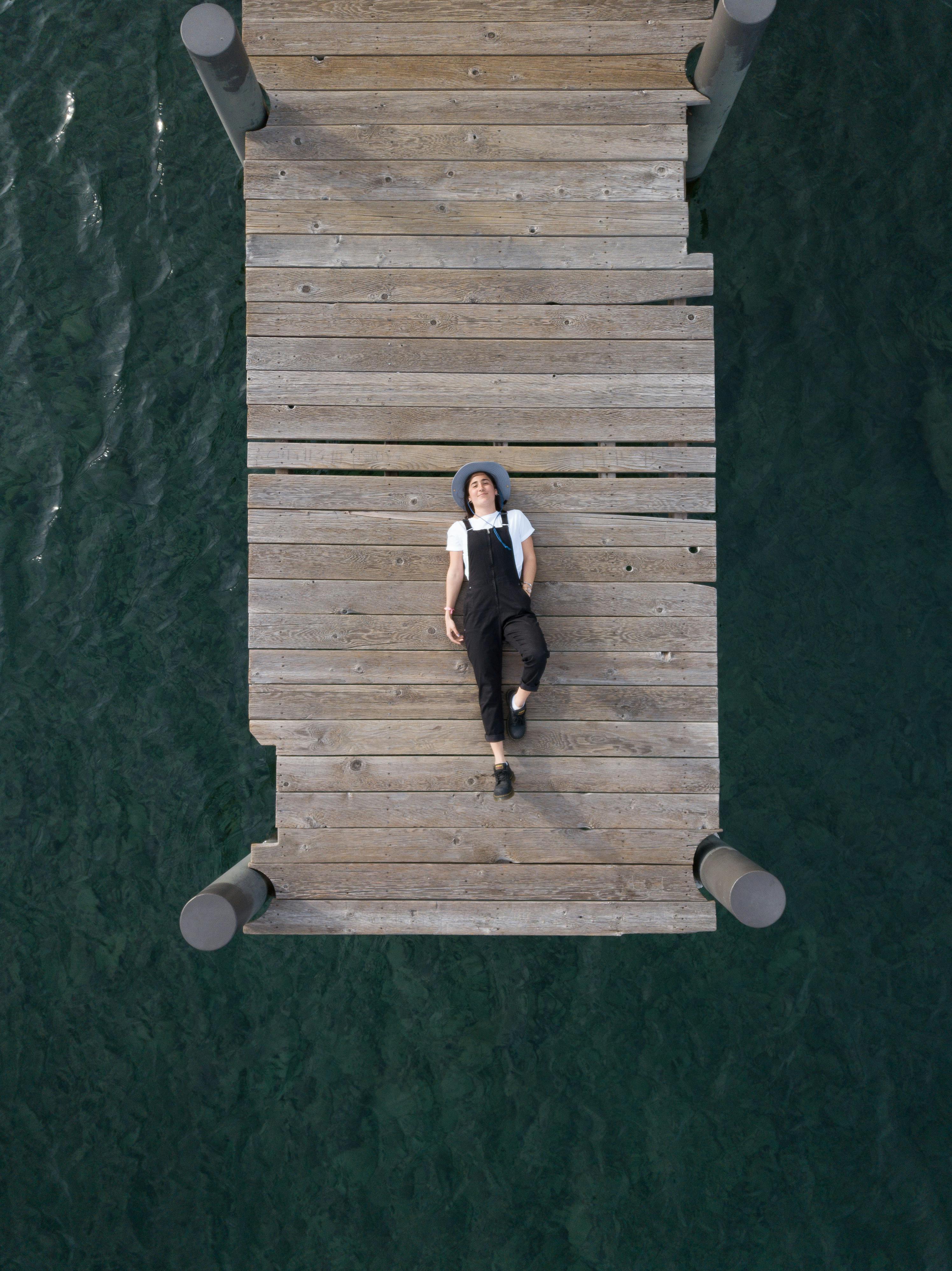 Woman In Black Overall Lying Down on Wooden Dock