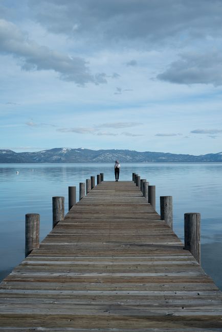 A serene scene featuring a person on a wooden dock overlooking a calm lake and distant mountains.