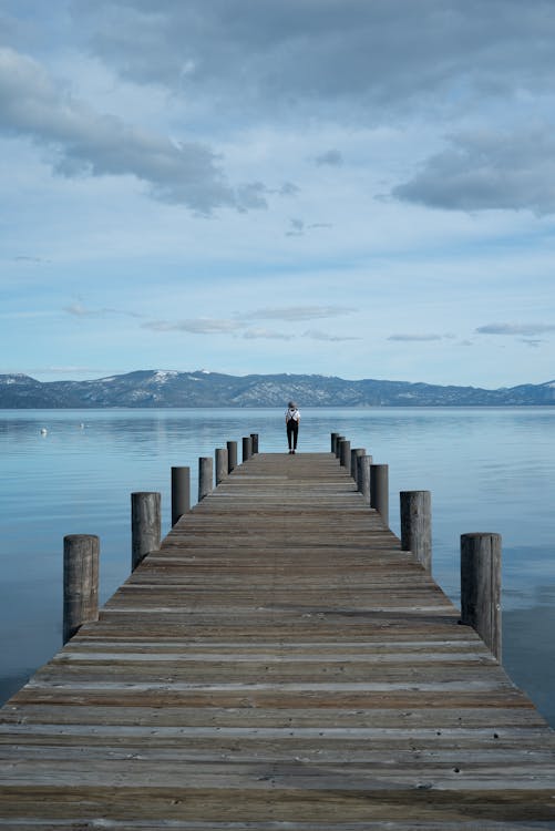 Person Standing on Brown Wooden Dock on Sea