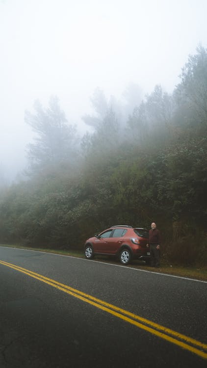 Traveler with car on foggy roadside