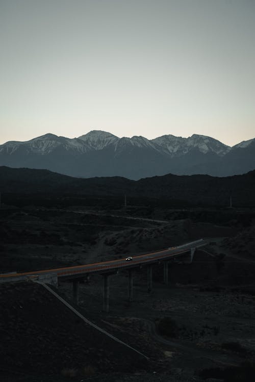 From above magnificent view of rough mountains with pointed peaks near narrow road with driving automobile under serene sky in twilight