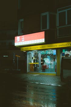 Rainy nighttime photo of an illuminated bakery entrance with vibrant signage and wet streets.