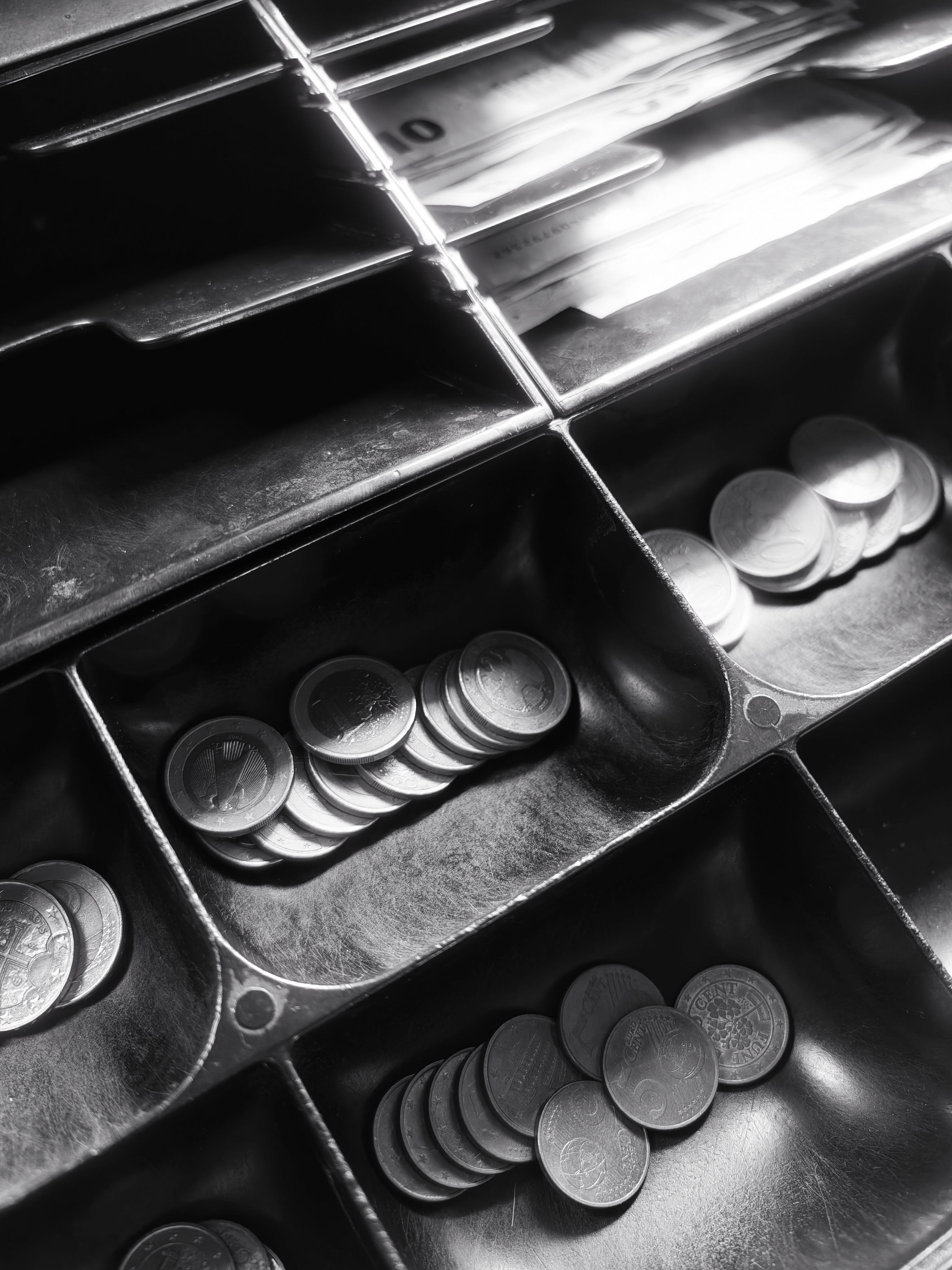 Black and white photo of cash drawers holding coins and bills in a classic register.