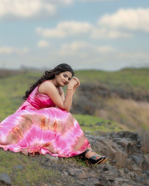 Free A woman in a vibrant pink dress poses gracefully on a rocky terrain under a bright sky. Stock Photo