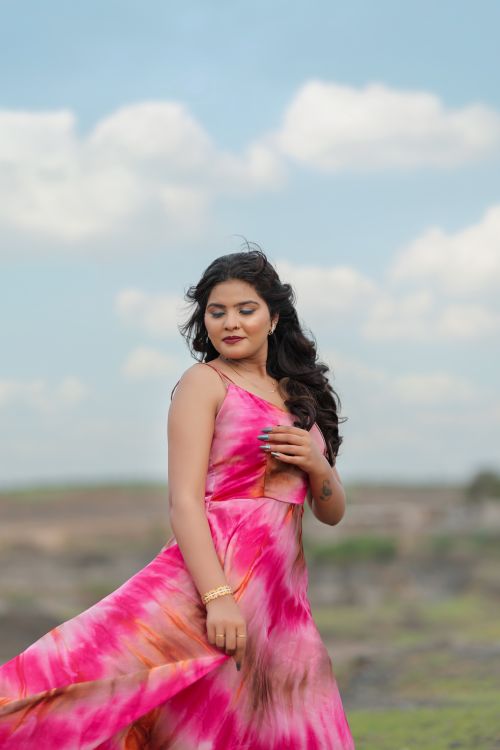 Free A woman in a pink dress poses gracefully against a bright blue sky. Stock Photo
