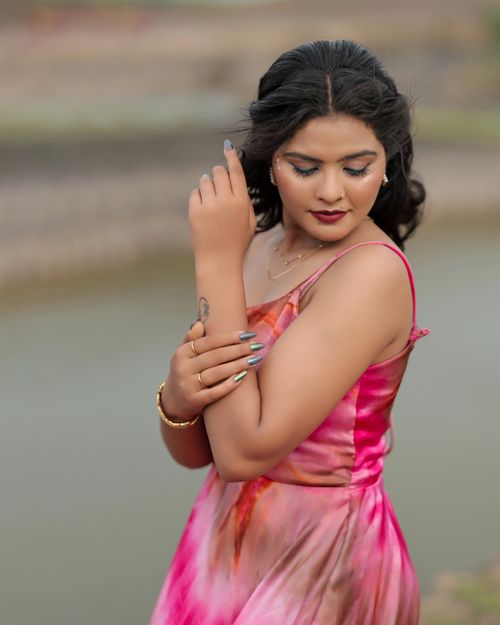 Free A poised woman in a vibrant pink dress stands gracefully by the riverside, showcasing elegant fashion and makeup. Stock Photo