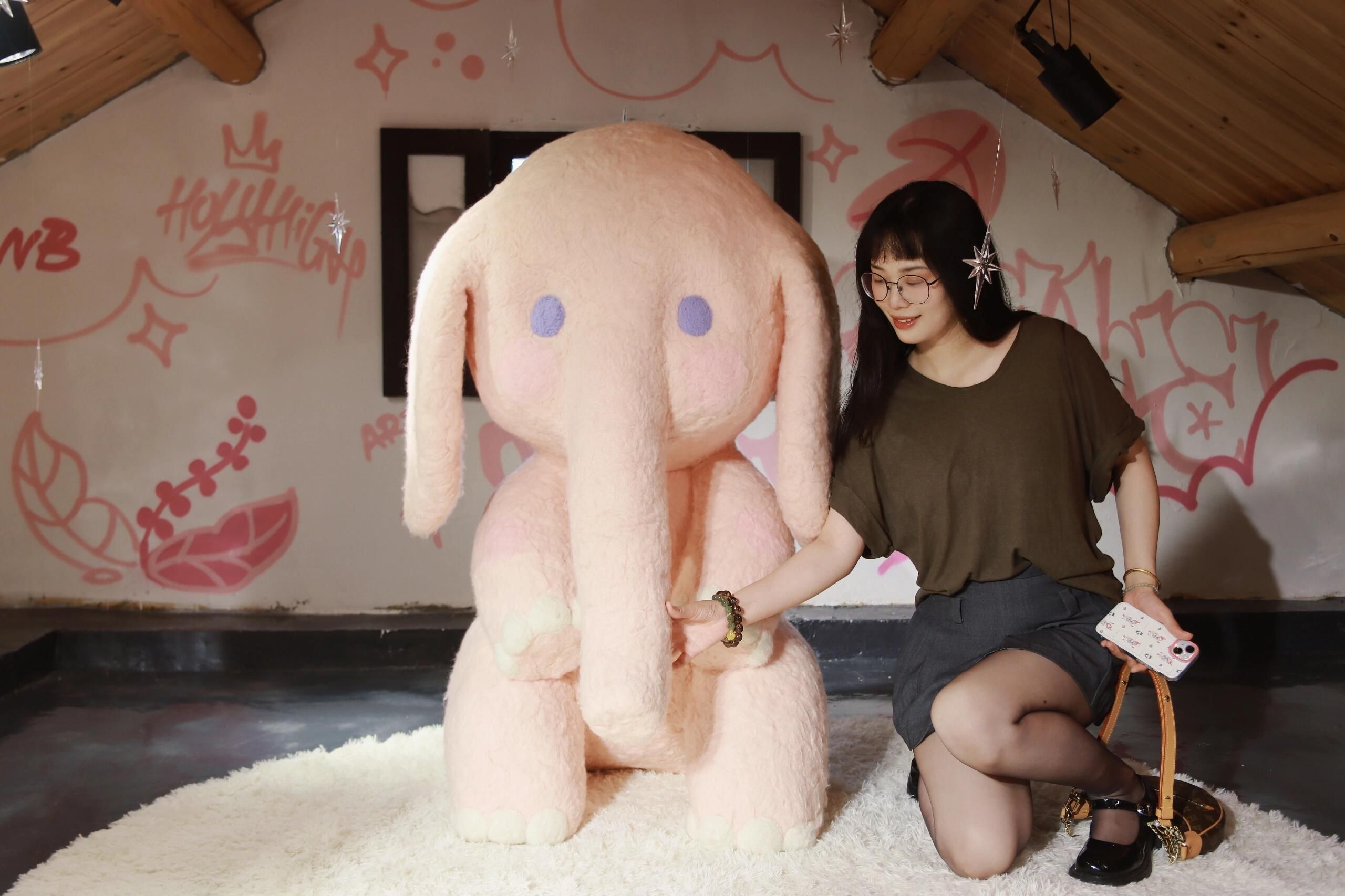 A young woman in a loft setting poses with a large plush elephant, surrounded by graffiti art. Photographed in Nanjing, China.