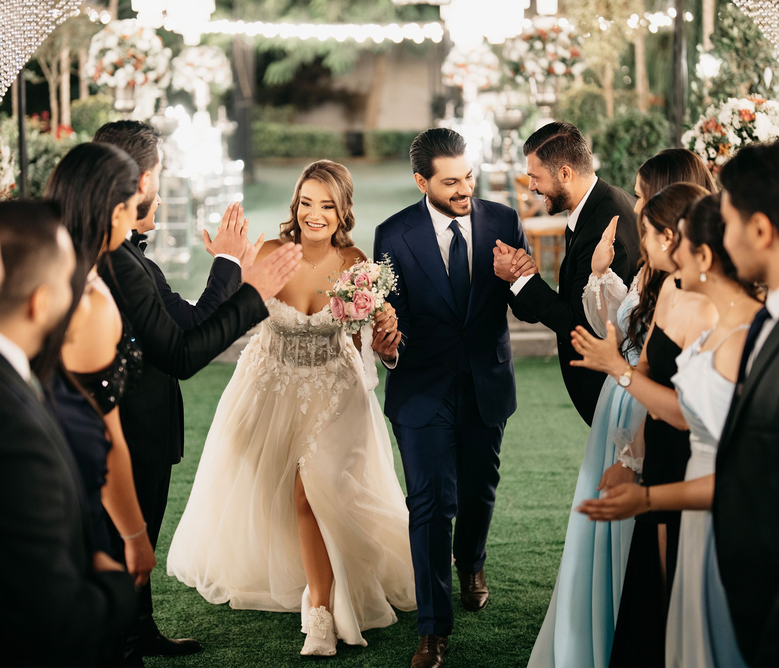 Bride and groom joyfully walking through cheering guests at a vibrant outdoor wedding reception.