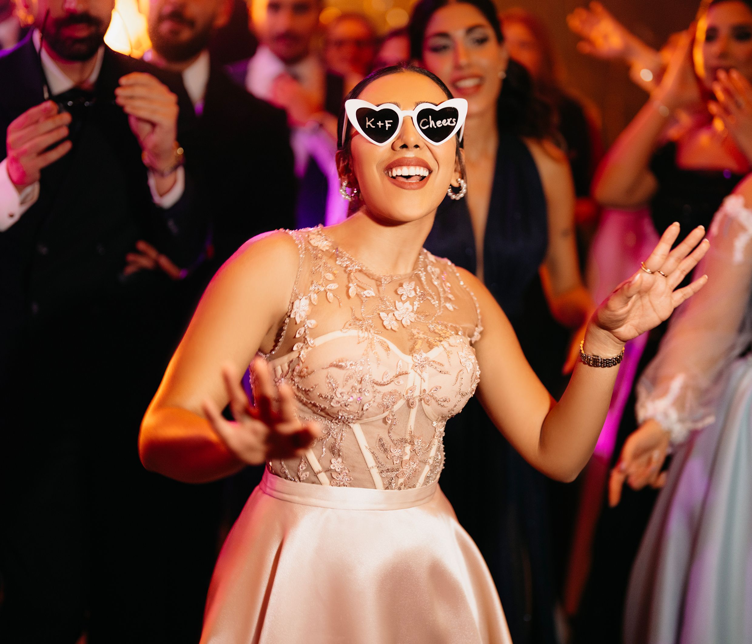 Elegant woman enjoys wedding reception wearing stylish sunglasses, surrounded by guests.