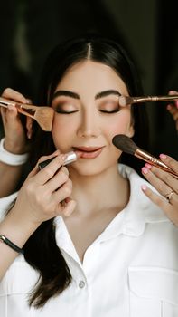 Close-up of a bride receiving a professional makeup look with various brushes and tools.
