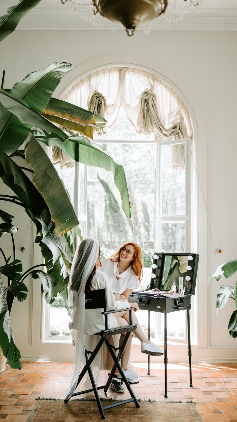 A bride in the artist's chair beneath a tall arched window, palms and a chandelier