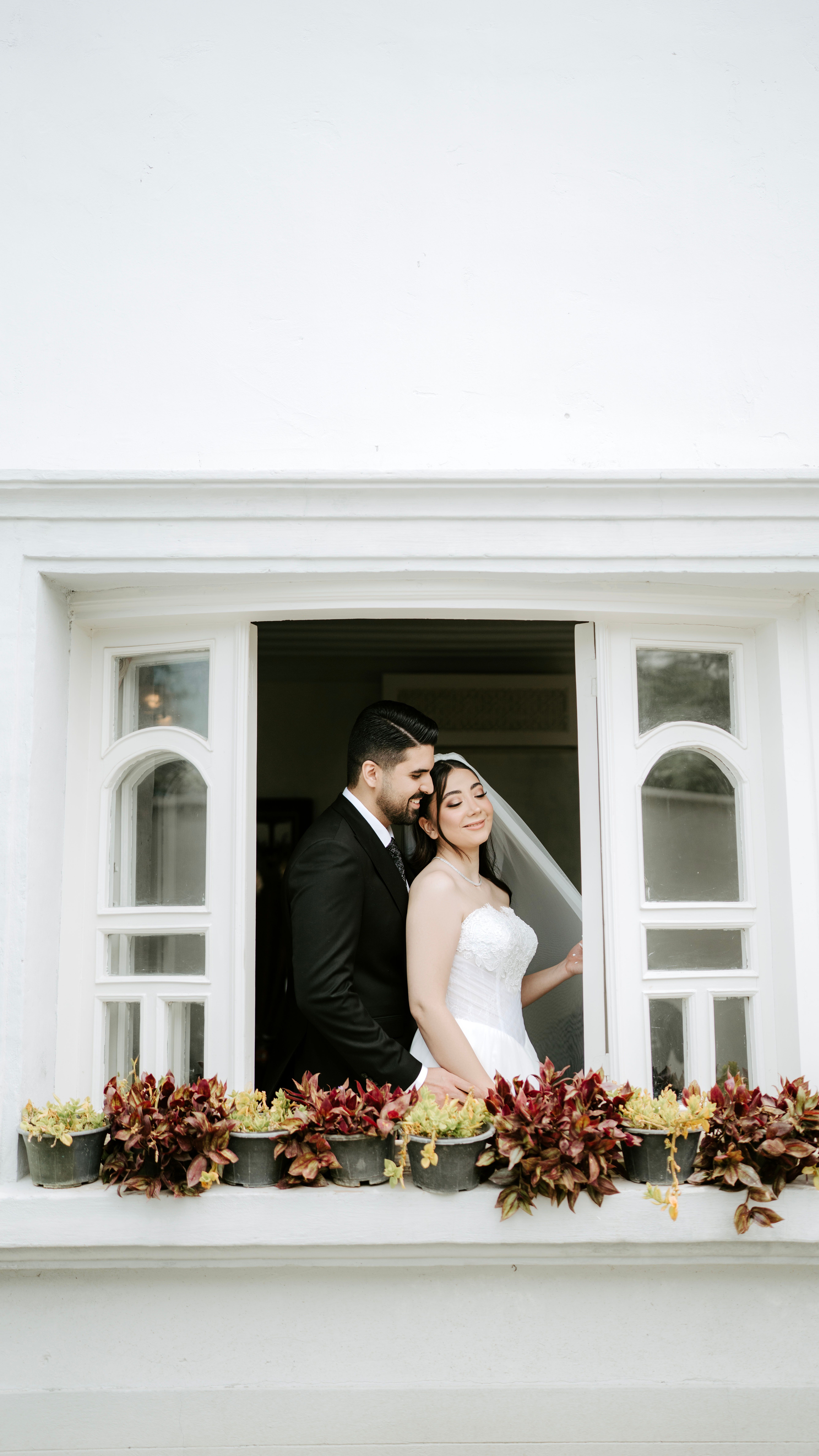 A beautiful bride and groom sharing a tender moment in a classic white archway, surrounded by flowers.