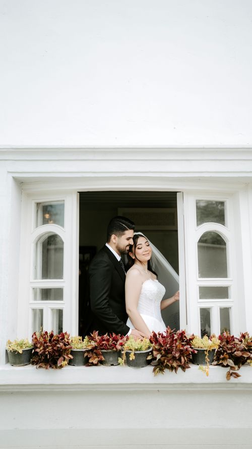 Free A beautiful bride and groom sharing a tender moment in a classic white archway, surrounded by flowers. Stock Photo