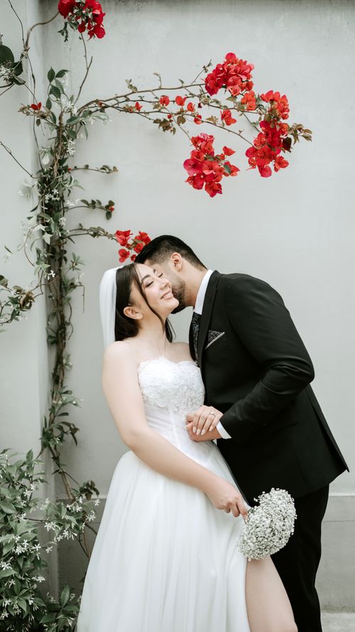 Free Bride and groom sharing a tender moment next to a vibrant bougainvillea backdrop. Stock Photo