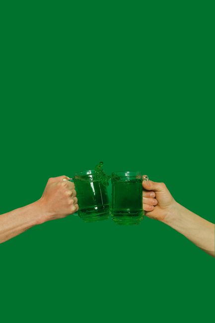 Two hands raise green beer mugs in a toast against a vibrant green background.