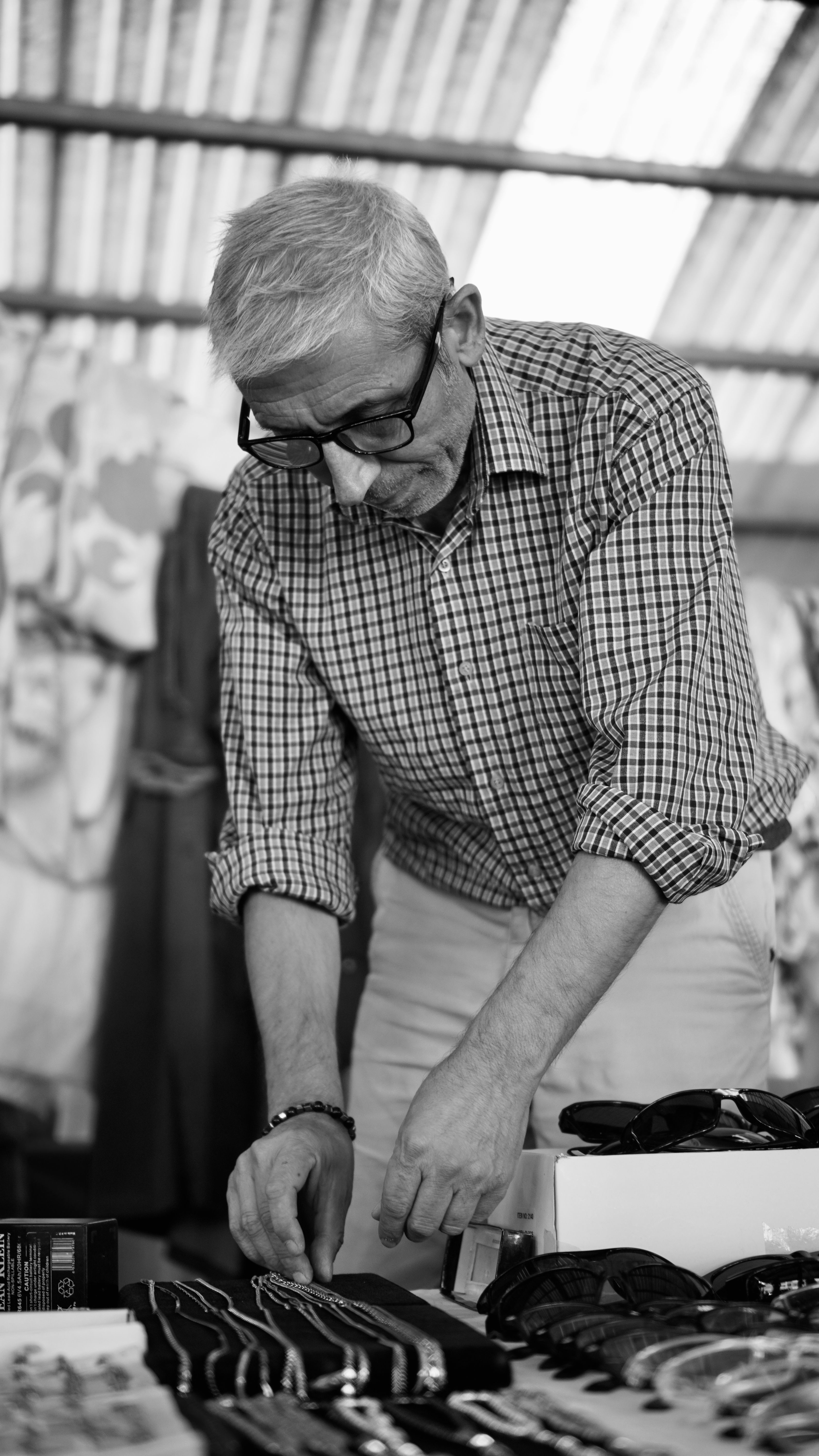 Senior man arranging items at a market stall in a black-and-white photo.