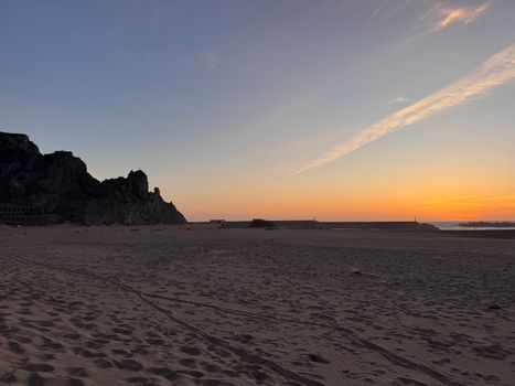 Serene beach scene in Sardinia, Italy at sunset with rocky formations casting shadows.