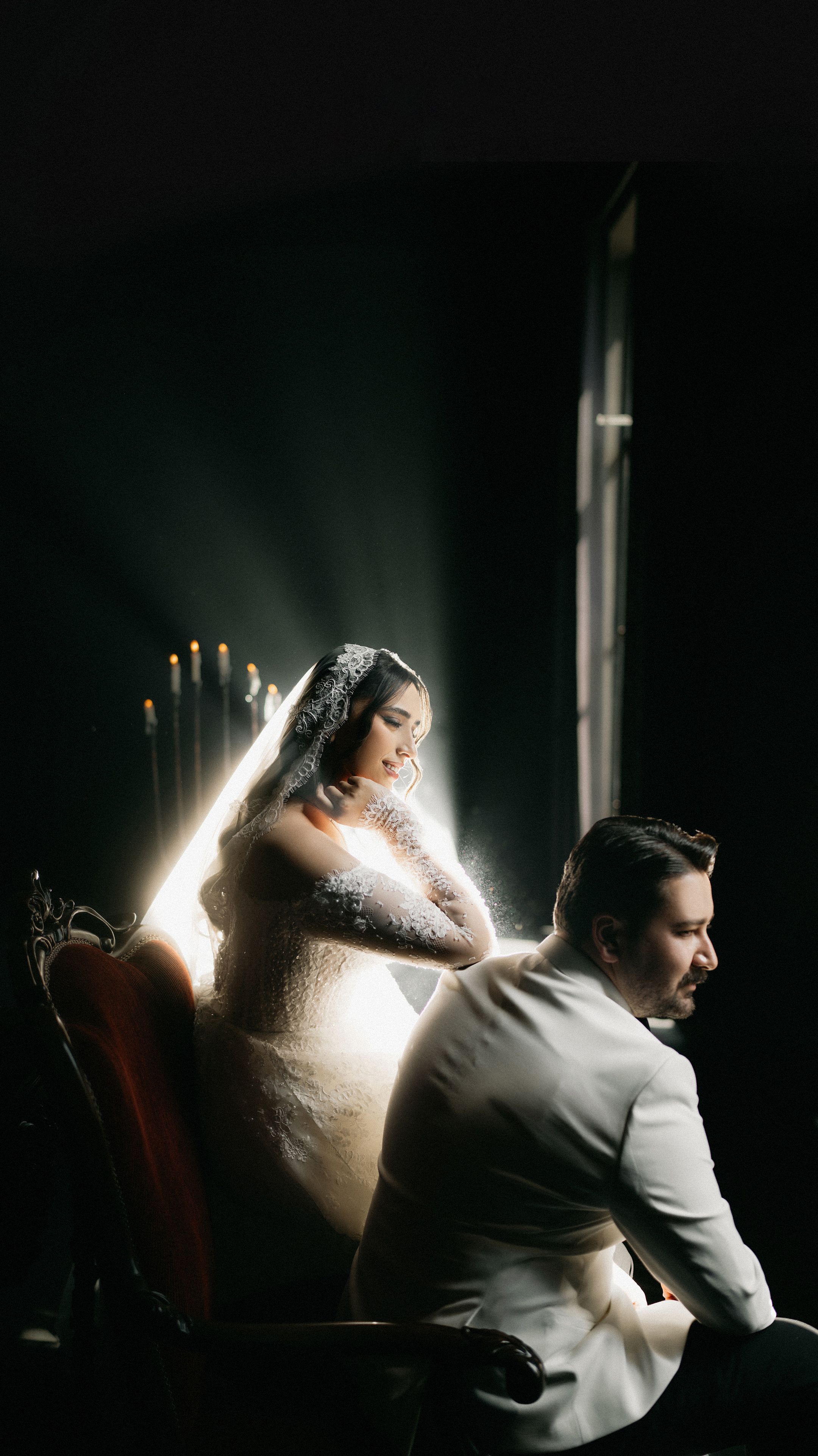 A bride and groom elegantly posed indoors with dramatic lighting, capturing timeless wedding elegance.