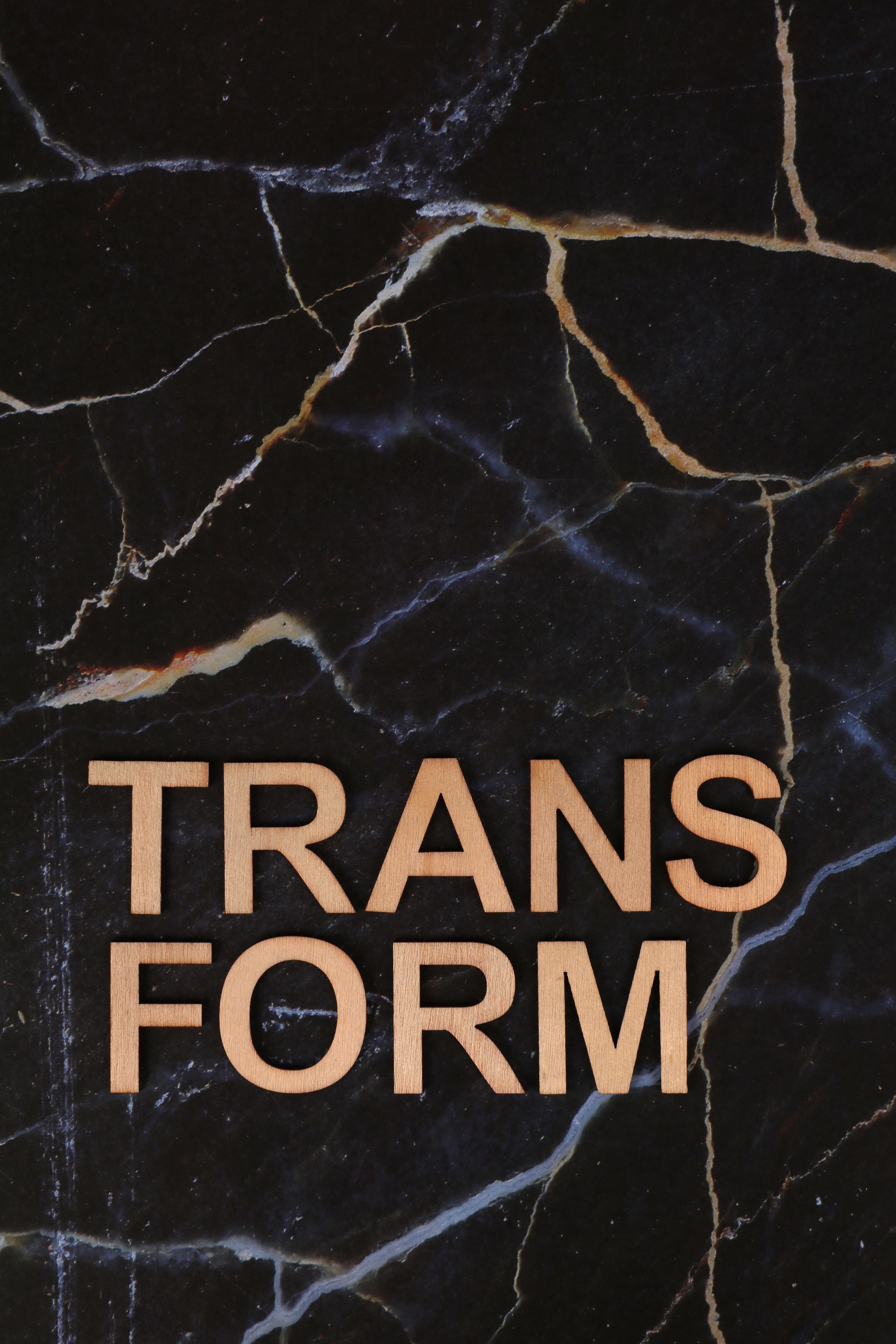 Wooden letters spelling 'TRANSFORM' on a black marble background.