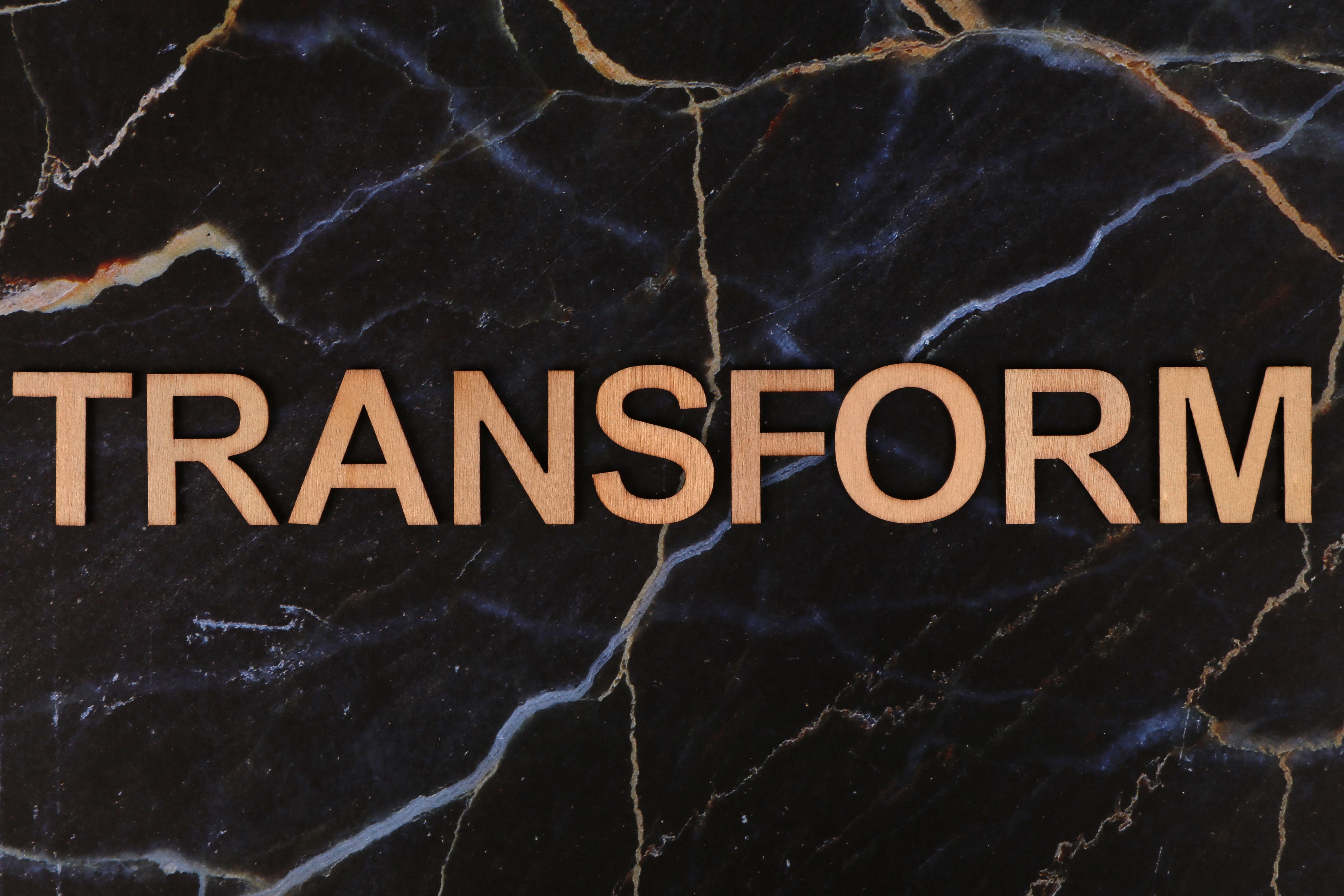 The word 'TRANSFORM' in wooden letters on a dark marble background, symbolizing change.