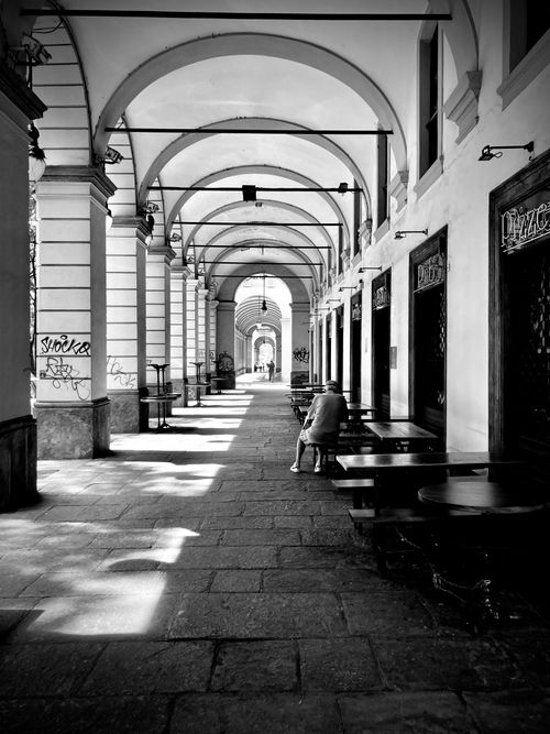 Free A serene black and white photo of an Italian alley with arches in Turin, capturing urban life. Stock Photo