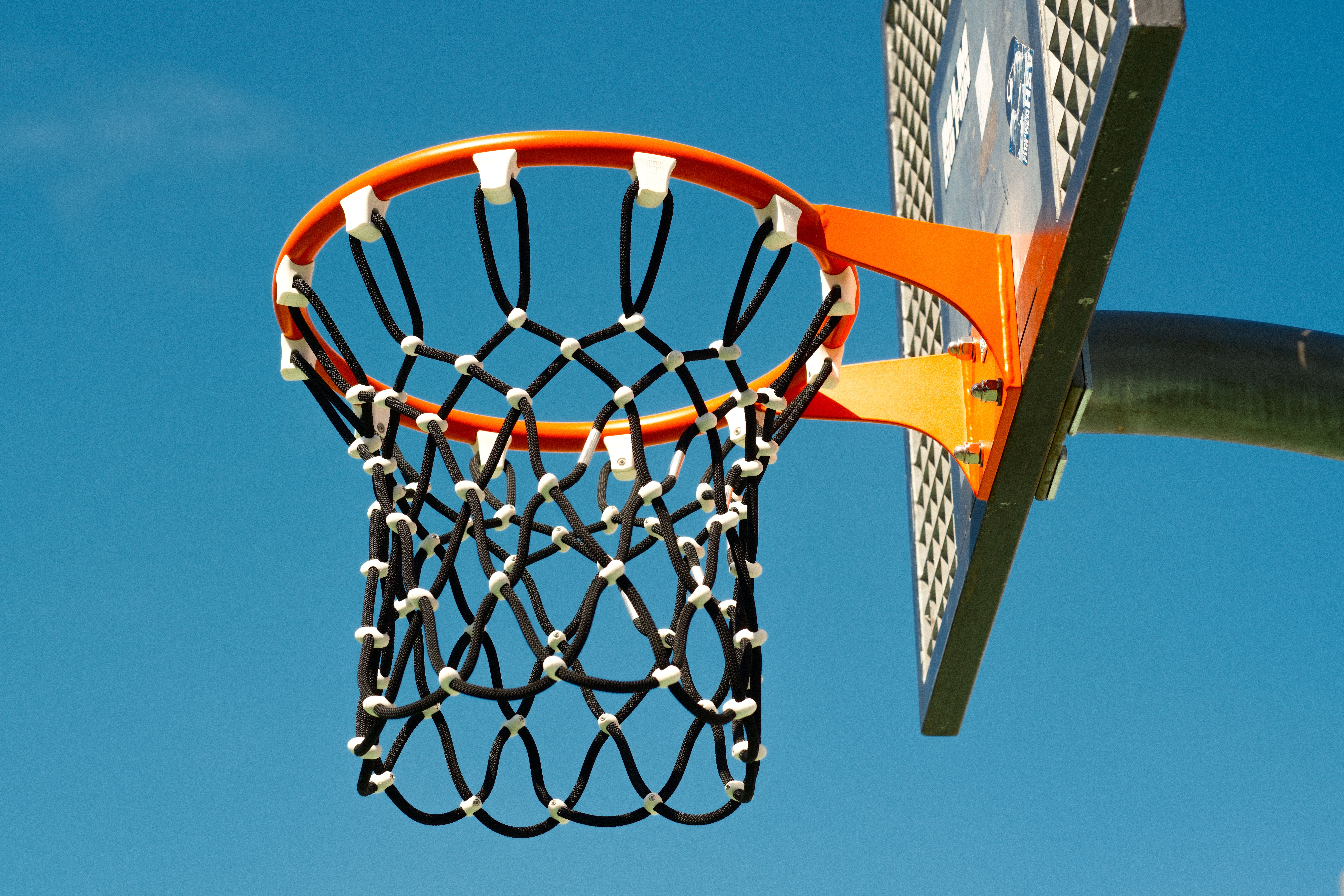 Close-up of a basketball hoop viewed from below against a clear blue sky, symbolizing sports and outdoor activities.