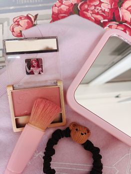 Stylish flat lay featuring pink makeup items and cute accessories on a floral background.