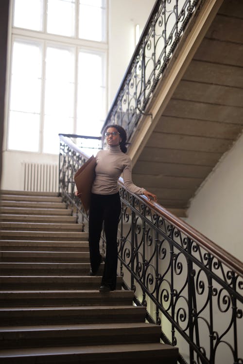 Woman in Gray Turtleneck and Black Pants Standing on Wooden Staircase