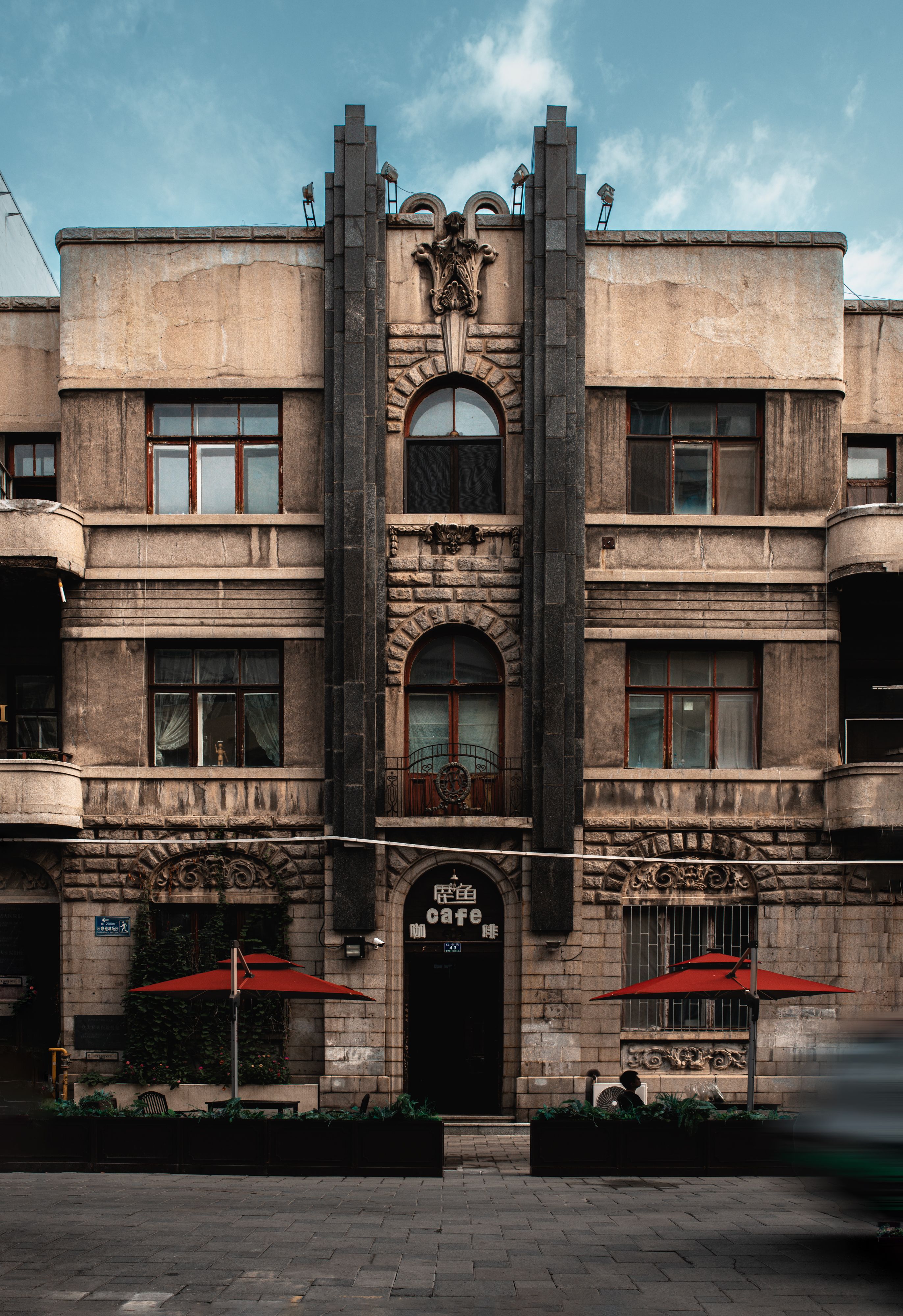 Front view of a historic Art Deco building with intricate architectural details and red umbrellas.