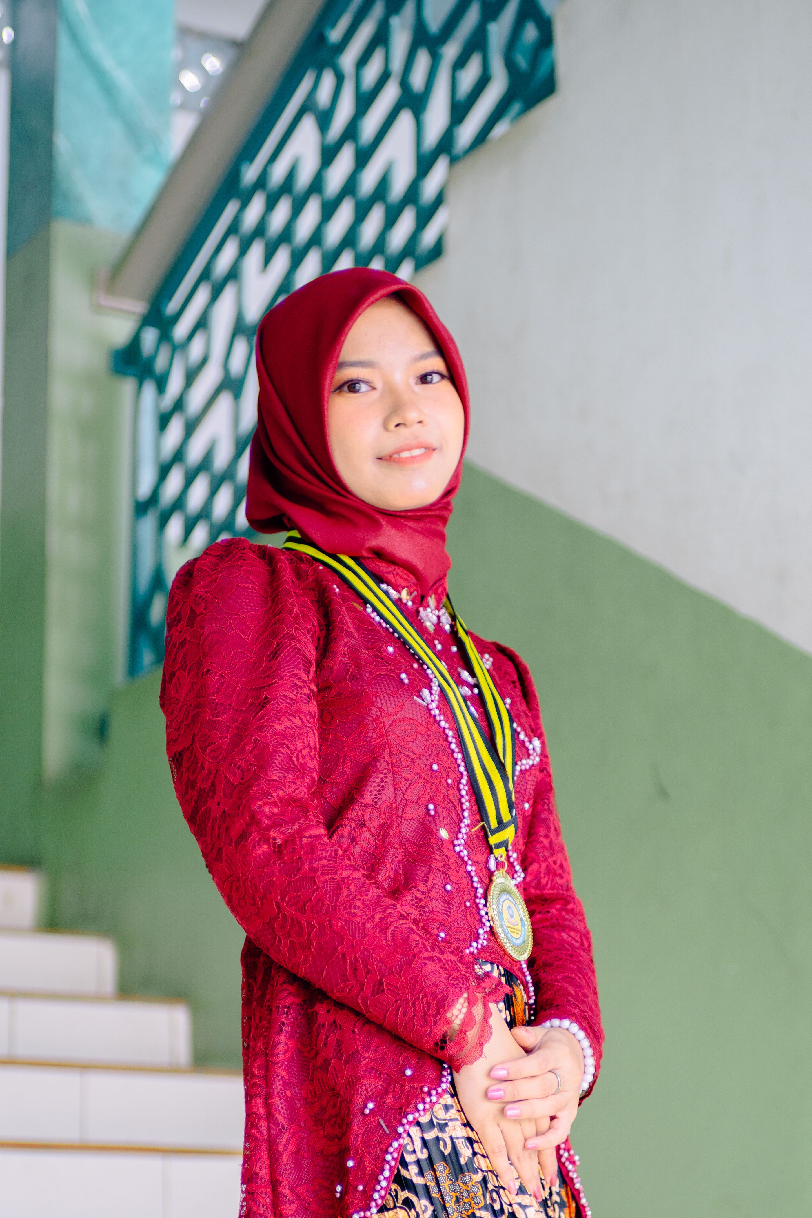 Young woman wearing hijab and traditional outfit with medal on stairs.