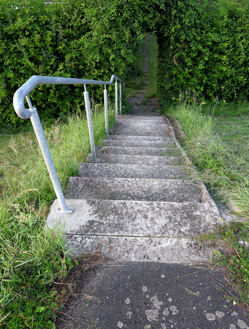 Free Concrete stairs with moss and handrail leading to a lush green path outdoors. Stock Photo